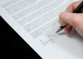 Close-up of a hand signing a formal document with a fountain pen, indicating agreement.