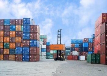 Colorful shipping containers and forklift in a busy Jakarta port under blue skies.