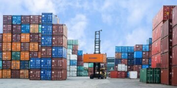 Colorful shipping containers and forklift in a busy Jakarta port under blue skies.